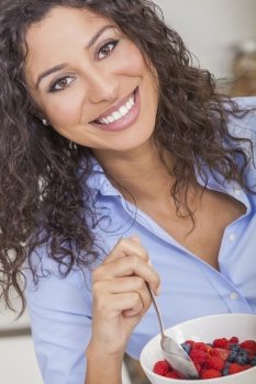 Beautiful, happy, young woman with perfect teeth, smiling & eating healthy fruit salad of strawberries, raspberries & blueberries in a bowl