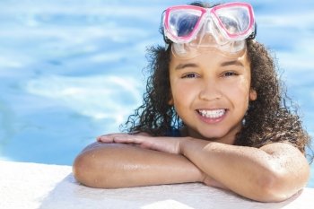 A cute happy young interracial African American girl child relaxing on the side of a swimming pool smiling & wearing pink goggles