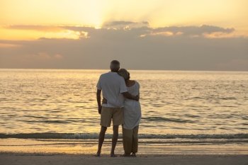 Senior man and woman couple embracing at sunset or sunrise on a deserted tropical beach 
