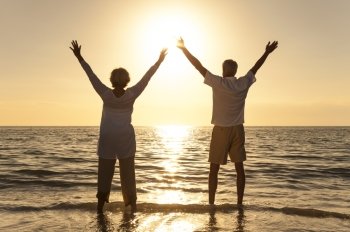 Senior man and woman couple arms raised celebrating together at sunset or sunrise on a beautiful tropical beach