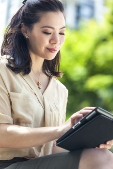 Happy, smiling, beautiful Asian Chinese business woman or businesswoman outside using tablet computer