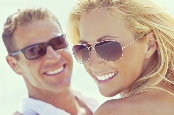 Instagram style photograph of happy and attractive man and woman couple wearing sunglasses and smiling in sunshine at the beach