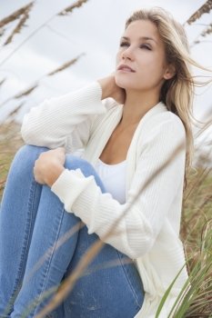 A beautiful blond woman or girl wearing jeans siiting in tall grass on a beach