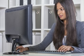 Portrait of a beautiful young Asian Indian woman or businesswoman in office typing using a computer