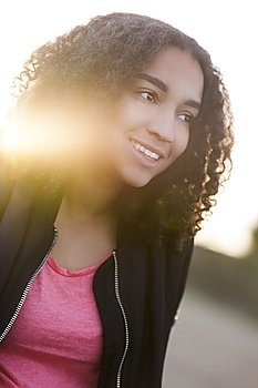 Outdoor sunset sunrise portrait with golden sunlight lens flare of beautiful happy mixed race African American girl teenager female young woman smiling with perfect teeth