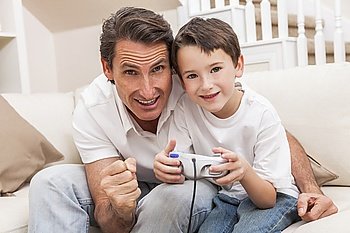 Man and male boy child, father and son having fun playing video computer console game together using handset controller on sofa at home