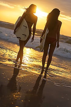 Rear view of two beautiful sexy young woman surfer girls in bikinis with white surfboards on a beach at sunset or sunrise