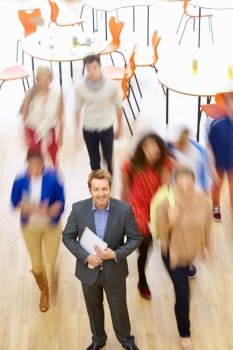 Male Tutor In Classroom Surrounded By Moving Students