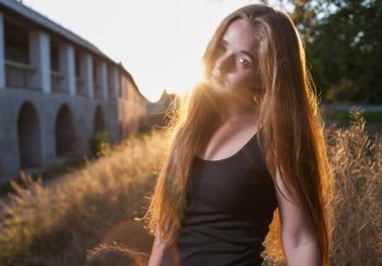 Young Woman In The Autumn Park at Sunset. Backlit. Picture of beautiful female over sunset, closeup portrait of romantic girl, attractive blond woman enjoying autumn golden sunlight, pretty young lady outdoors rejoice of warm weather at fall season