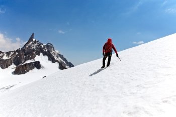 Climber standing on a glacier looking at a mountain peak. Dent du Geant, Mont Blanc, Chamonix, France.