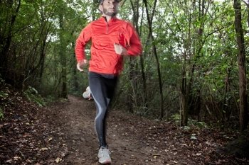 Male trail runner running in the forest on a trail. Red shirt and black pants. Summer season. Slight blur in runner to show motion. Horizontal composition.. Cross country running