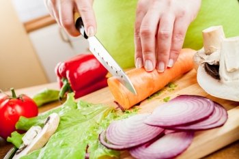 Woman’s hands cutting carrot, behind fresh vegetables.