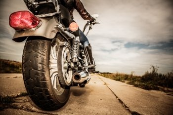 Biker girl riding on a motorcycle. Bottom view of the legs in leather boots. Focus on the rear wheel.