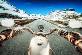 Biker rides a motorcycle on a slippery road through a mountain pass in Norway. Around the fog and snow. First-person view.