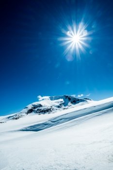 Sun in a blue sky over snowy mountain.