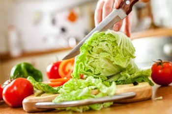 Woman’s hands cutting lettuce, behind fresh vegetables.