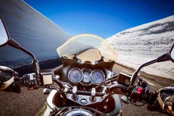 Biker rides a mountain road with high snow wall in Norway. First-person view.