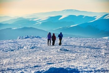 People walking at sunset in winter mountains covered with snow
