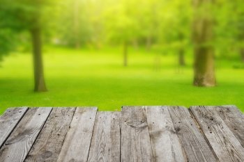 View from empty wooden deck table to the green spring foliage bokeh background