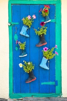 Old children rubber boots with blooming summer flowers on the entrance door of a house