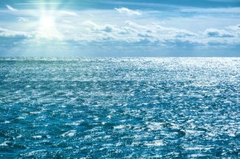 Blue sea with sky, sun rays and clouds. Water natural background