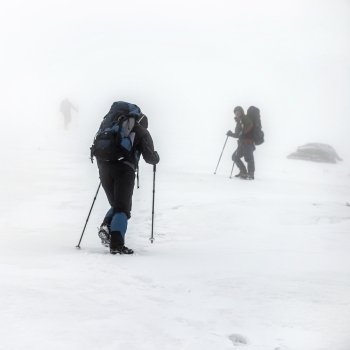Mountain hiking group with backpacks and trekking poles having hard climbing trip in winter snow storm