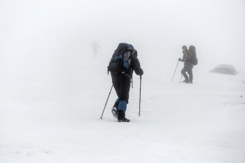 Mountain hiking group with backpacks and trekking poles having hard climbing trip in winter snow storm