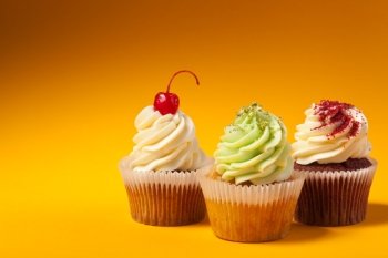 three cupcakes isolated on orange background with copyspace