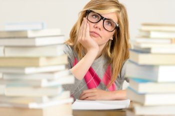 Bored student girl between stack of books looking up glasses
