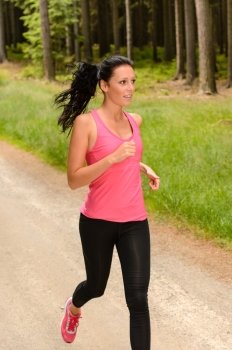 Sportive woman running through forest on summer training day