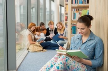 Young student sitting in college library with friends in background