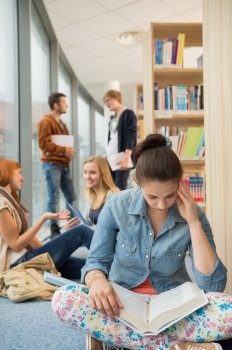 Girl reading book with group of students discussing in library