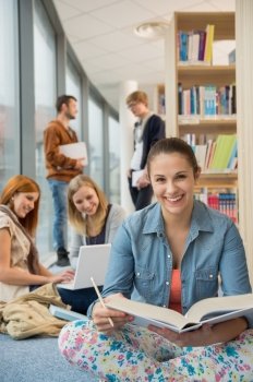 Happy student with classmates in background sitting in school library