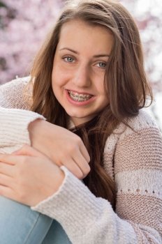 Smiling teenage girl with braces hugging knees outdoors