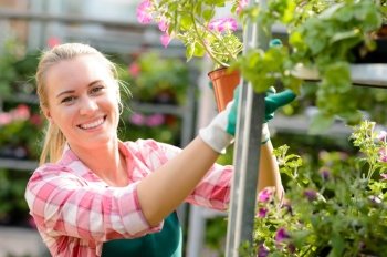 Smiling woman working in garden center with potted flowers sunny