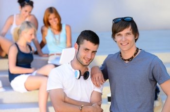 Two student boys standing outside college summer friends in background