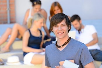 Smiling student boy with friends outside college holding books summer