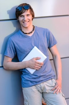 Smiling student boy with tablet leaning against modern wall