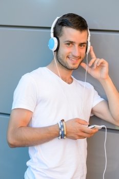 Smiling student boy with headphones standing by modern college wall