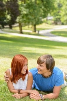 Teenage couple lying sunny park grass looking at each other