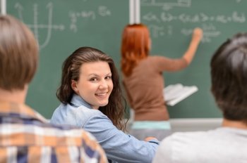 Smiling student girl sitting front of chalkboard during mathematics lesson