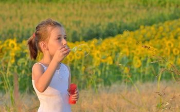 Little girl blowing soap bubbles on field
