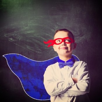 school boy wearing a superhero costume with blackboard behind him