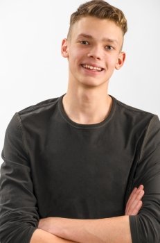 portrait of a teenager. portrait of a happy male caucasian teenager with folded hands on gray background 