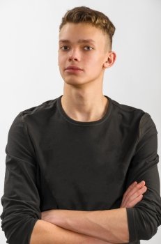 portrait of a teenager. portrait of a happy male caucasian teenager with folded hands on gray background 