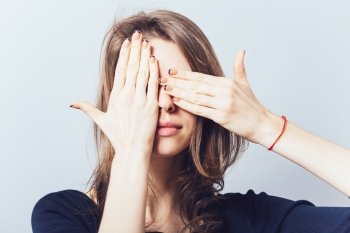 Young teen woman covering her eyes isolated on a gray background