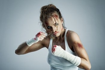 A photo of woman standing in fight position with blood over the face and fists.