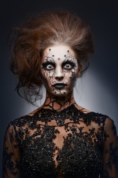 A girl standing like a statue in a creepy halloween costume of a witch with peircing and cracked face paint.