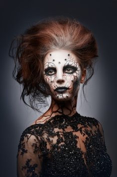 A girl posing in a creepy halloween costume of a witch with peircing and cracked painted face.