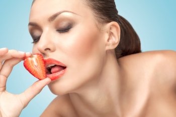 A beautiful girl licking a red juicy strawberry with a temptating tongue.